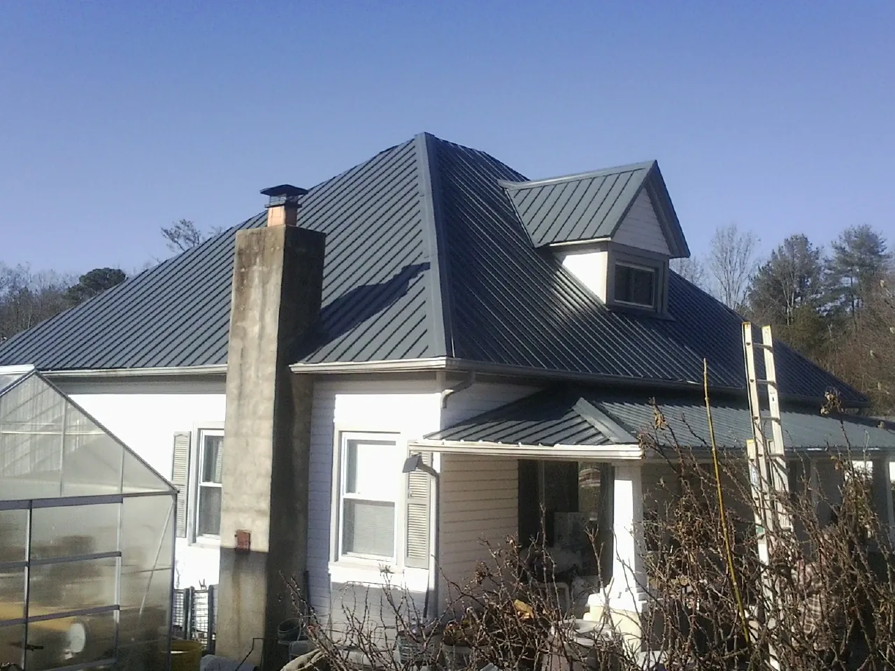 Dark blue standing seam metal roof on a white farmhouse with dormer — Slate & Tile Roof Repair by Roofing Brothers in Canton Center
