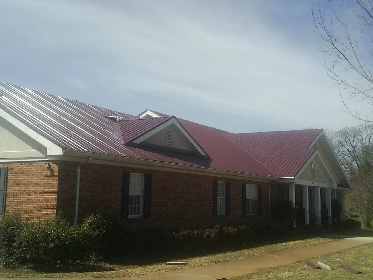 Red metal roof with gabled entries on a long brick building, from a Hail Damage Roof Repair job in Canton Center