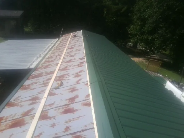Old rusted panels beside newly installed green metal roofing — Wind Damage Roof Repair by Roofing Brothers in Canton Center