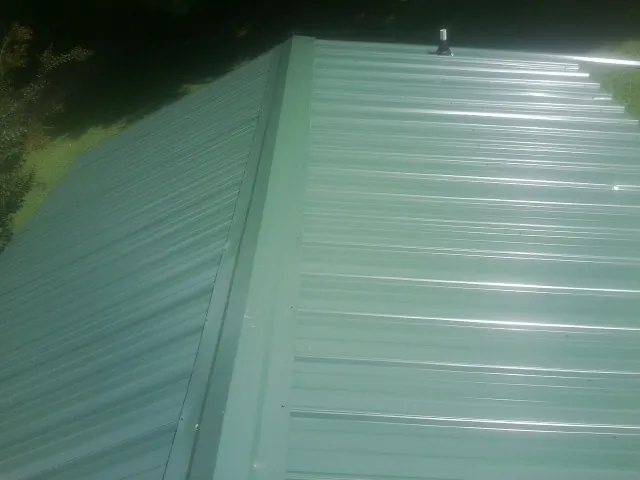 New green metal panels meeting at the ridge of a roof — Flat Roof Repair work by our crew in Canton Center