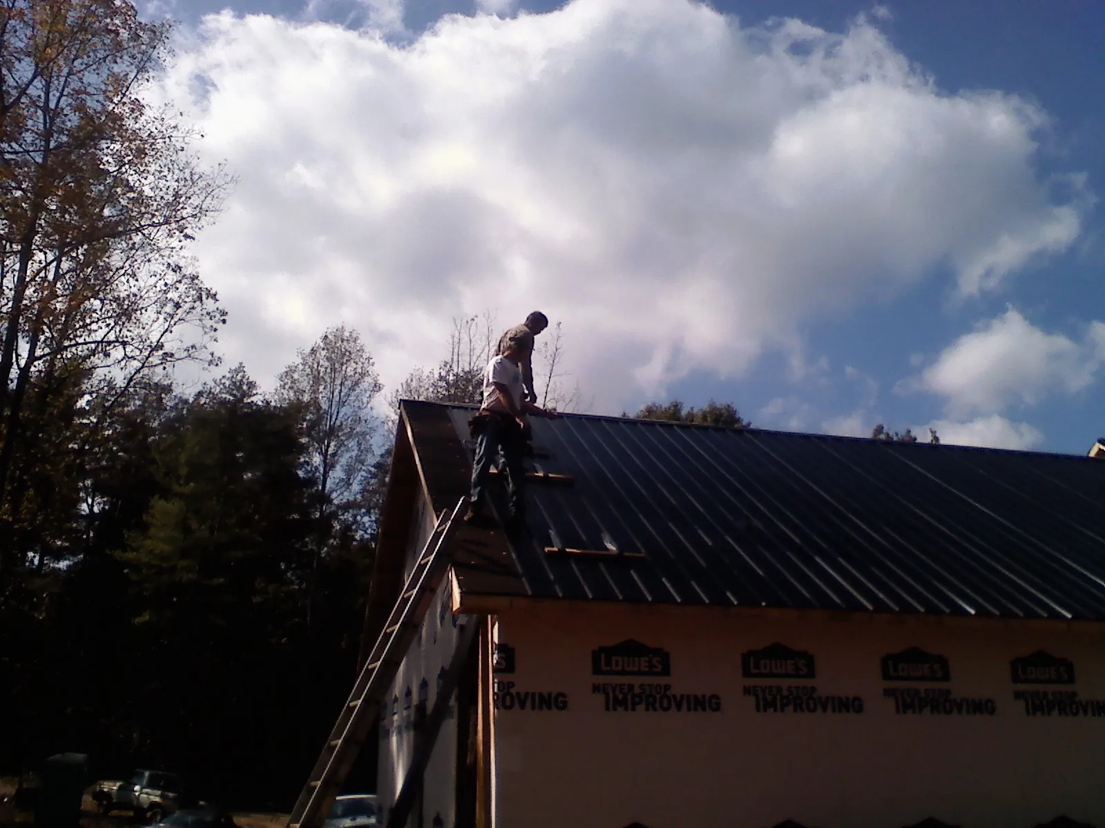 Roofer fastening dark metal panels high against a cloudy sky, from a Roof Inspection job in Canton Center