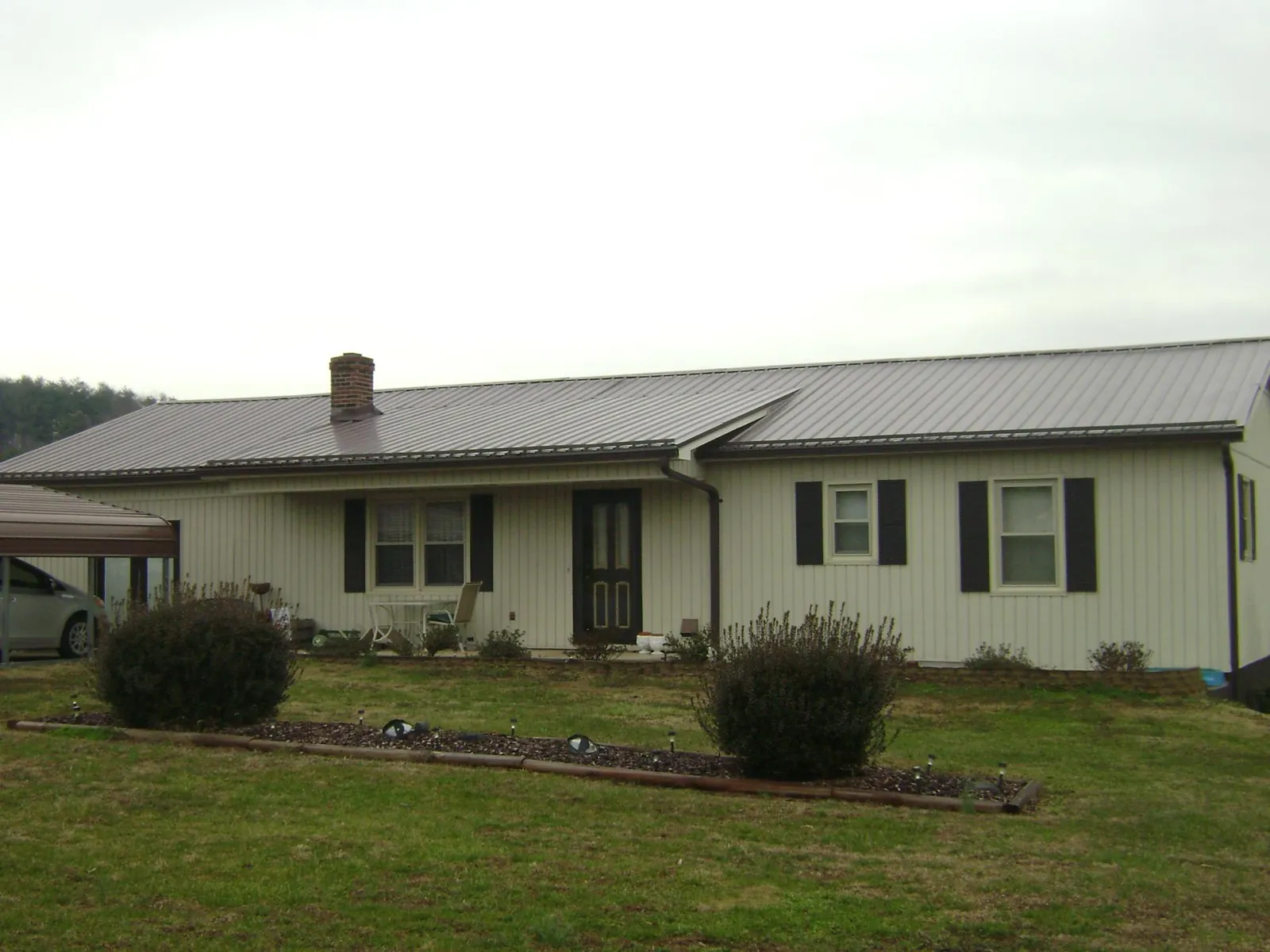 Brown metal roof on a cream sided ranch home with a brick chimney in Canton Center