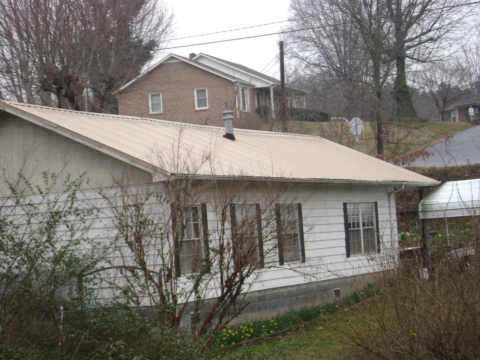 Tan metal roof on a white sided house set into a hillside — Commercial Roofing by Roofing Brothers in Canton Center