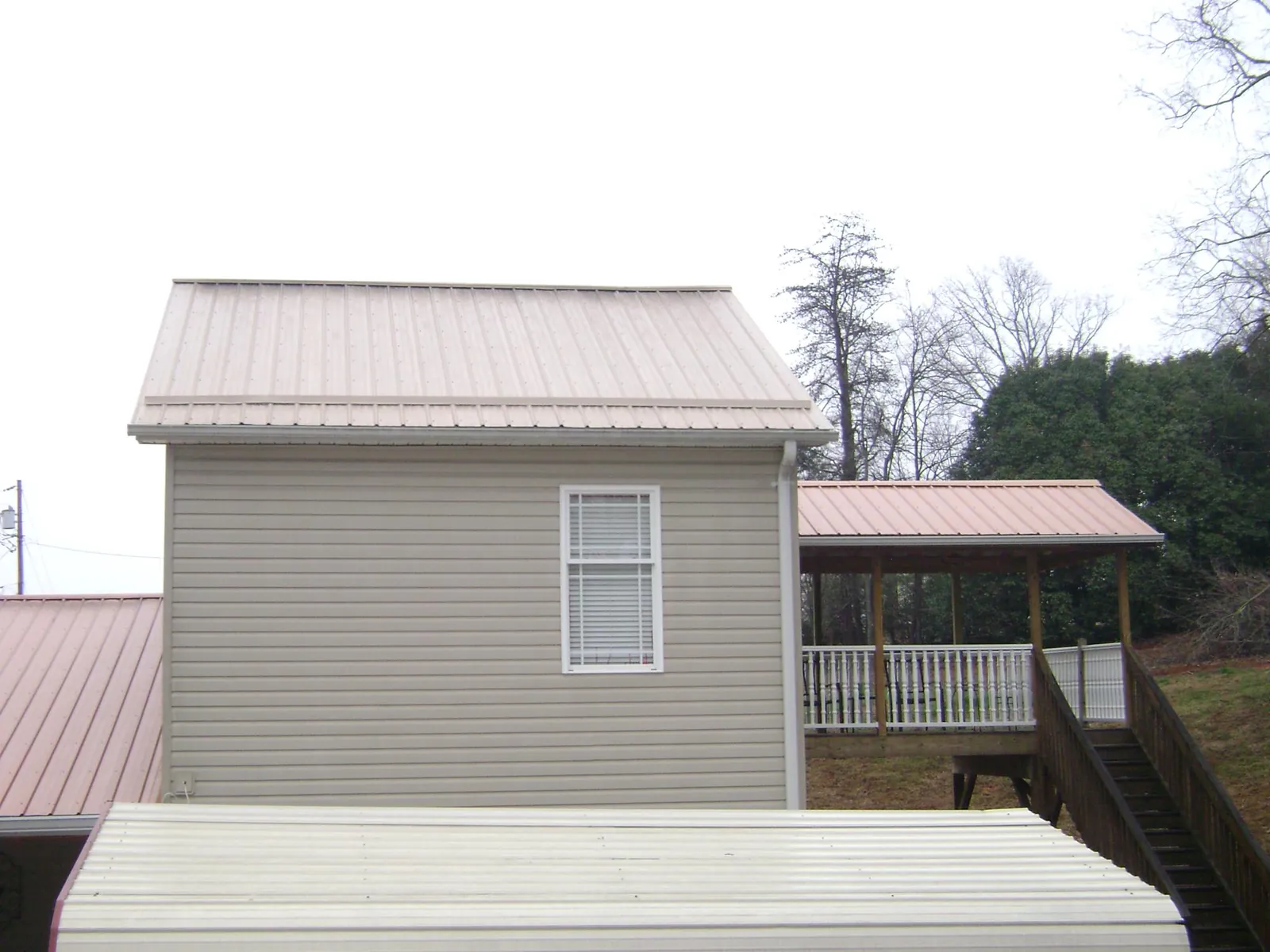 Tan metal roofs on a two story addition and attached porch, from a Roof Replacement job in Canton Center